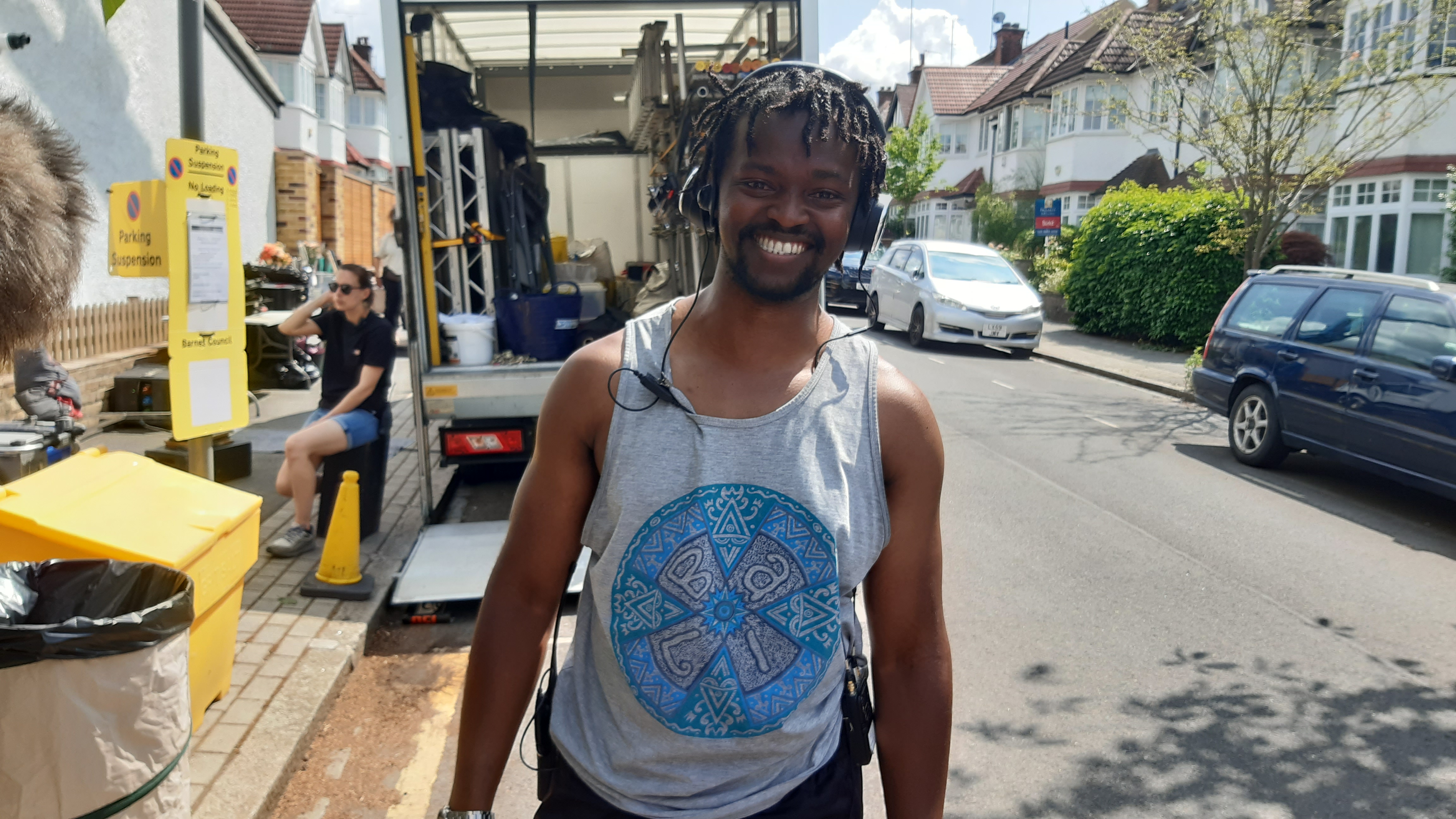 A sound trainee smiles at the camera while wearing a headset on a residential London street on production of film, Hard Truths