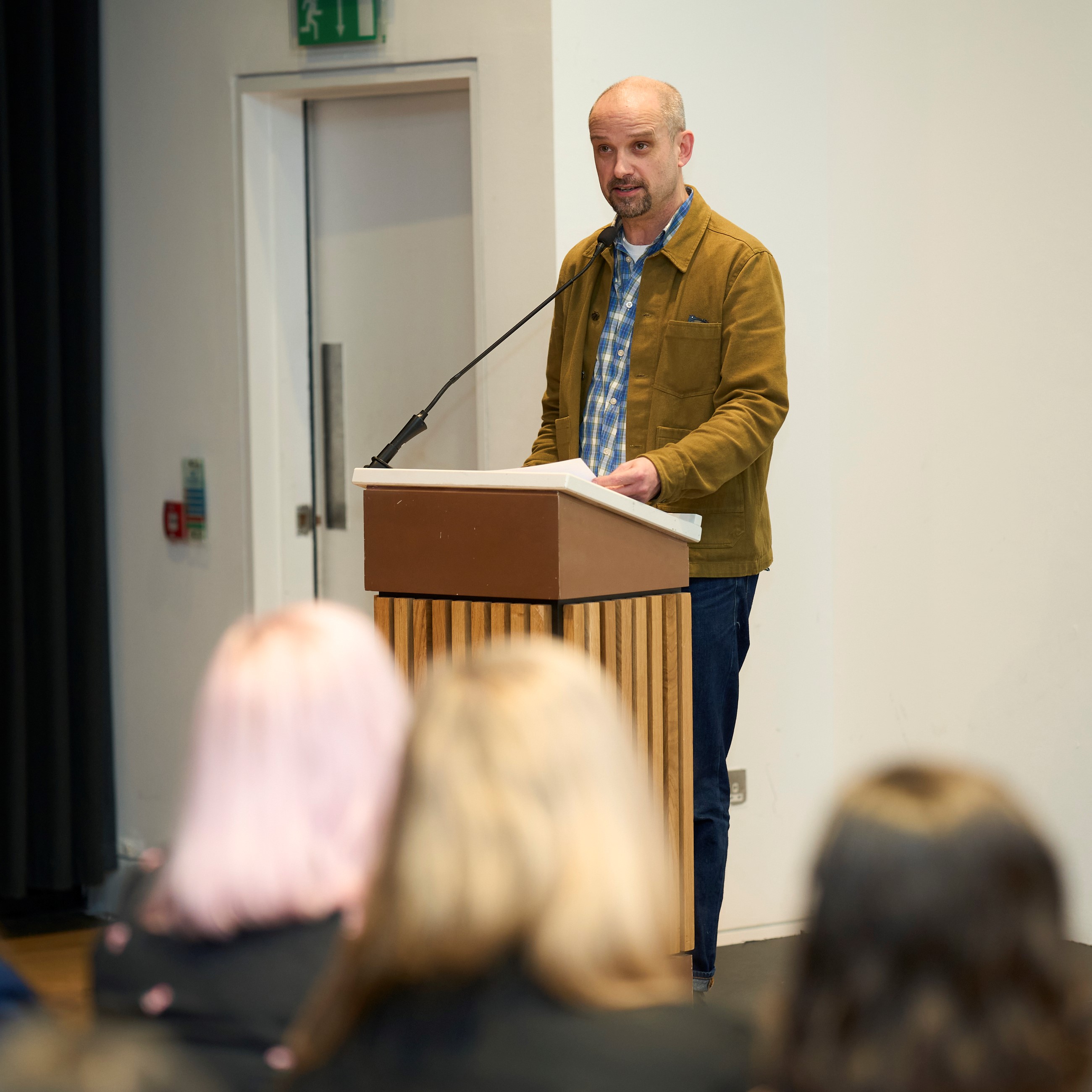 Barry Ryan wears a mustard overshirt as he stands behind a lectern to deliver a speech in front of a crowd